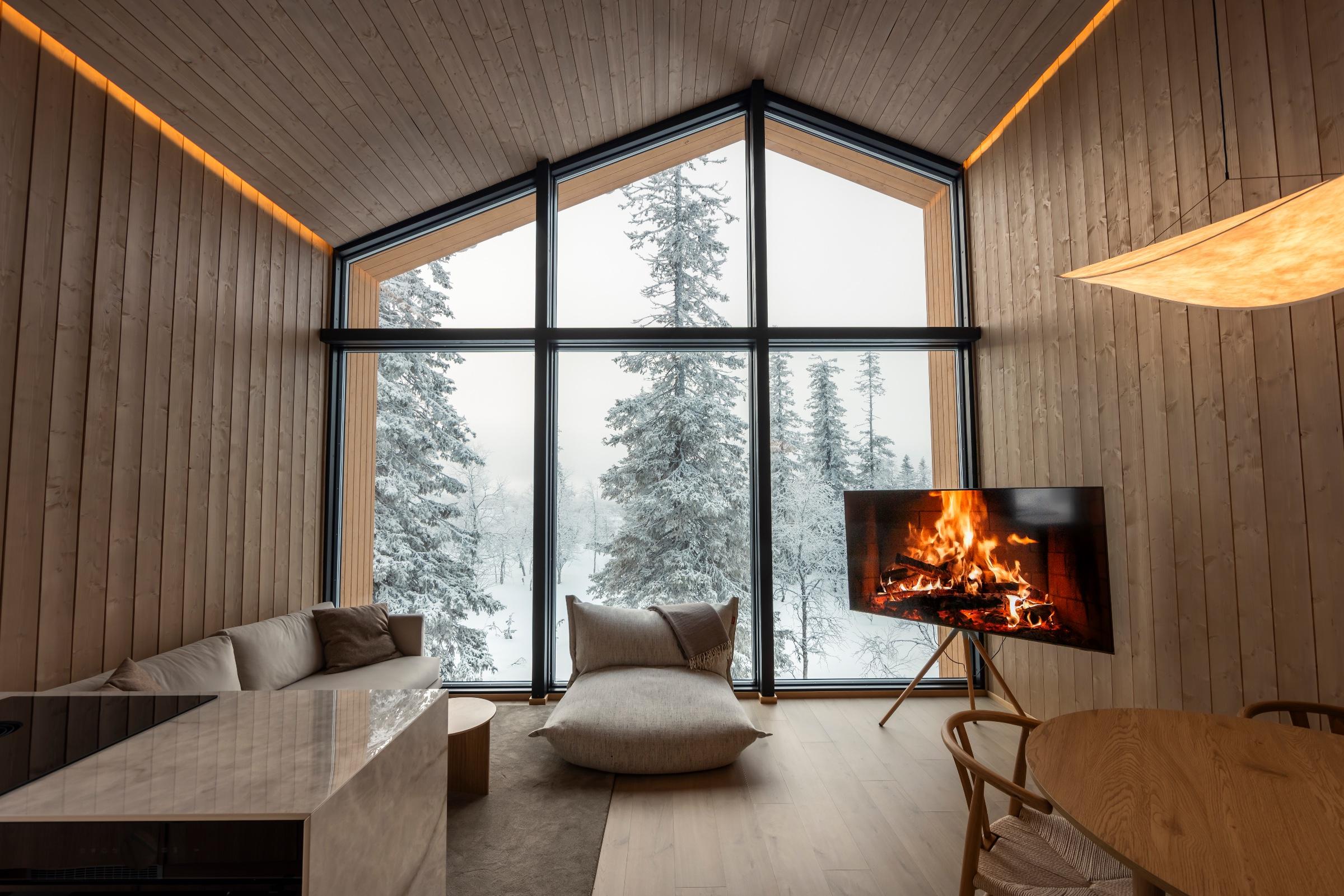 Lit glass igloos scattered through a snowy forest under the northern lights, from the air